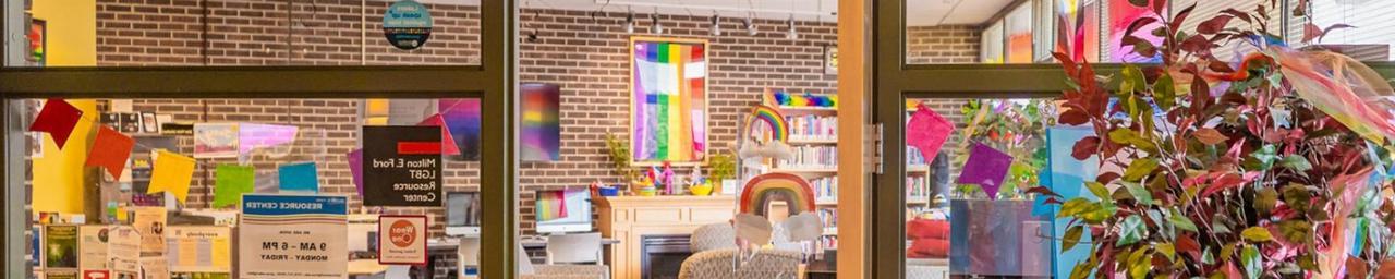 Looking through the door and glass windows of the LGBT Resource Center. It is bright and colorful inside, with a visible rainbow flag. Photo credit: Macayla with Lanthorn 2022